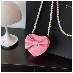 Detailed macro view of pink heart-shaped bag with bow decoration and pearl chain