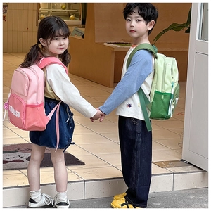 Two young children wearing pink and green backpacks with front pockets and side mesh