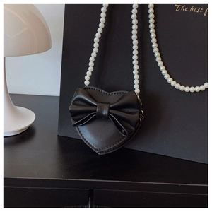 Detail of black heart-shaped kids crossbody bag with leather bow and pearl strap