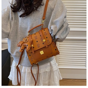 Detail of a brown leather backpack with logo patterns and a cute dog pendant accessory