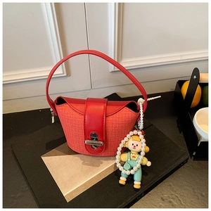 Close-up of red woven bucket bag with leather flap and pearl cartoon doll charm