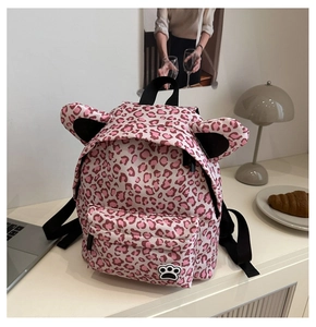 Pink leopard print kids backpack with 3D cat ears and paw print detail on white desk
