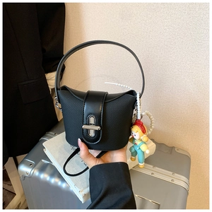 Detail of black bucket bag featuring textured fabric and decorative pearl cartoon pendant