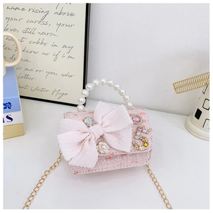 Pink tweed mini bag with pearl handle, large bow, and jeweled charms on a white table