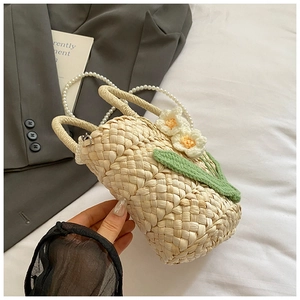 Detailed close-up of straw bucket bag with knitted flowers and pearl chain strap