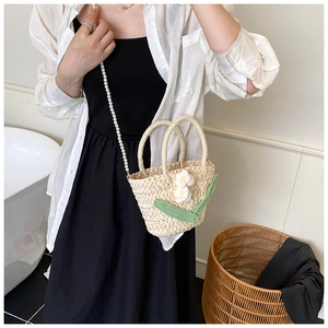 Detail of straw woven bag with floral knit decor and elegant pearl chain strap
