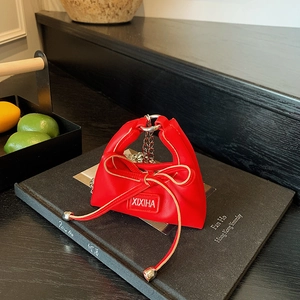 Detail of red mini handbag with bow and chain strap on a textured book surface