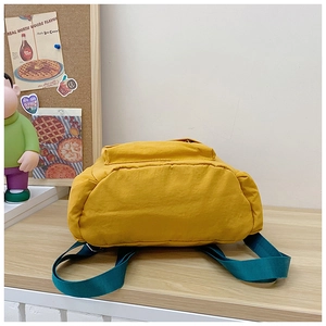 Close-up of mustard yellow canvas backpack with dark green woven straps on wooden desk