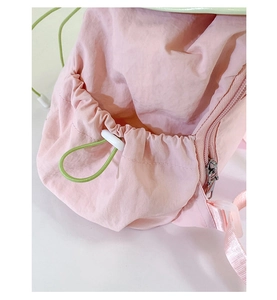 Close-up of pink backpack showing green drawstring with white toggle and side zipper detail.