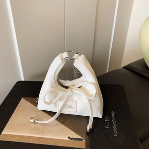 Detail of a white mini handbag featuring a large bow and metallic ring handle decoration