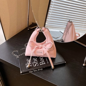 Pink mini chain bag with bow and metal ring handle displayed on a mirror base