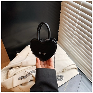 Détail d'un mini sac noir en forme de cœur avec bandoulière chaîne argentée et poignée