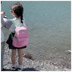 Pink nylon kids backpack with neon green straps shown in an outdoor scenic view