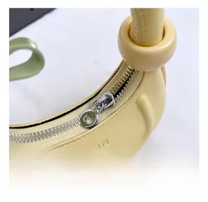 Detail of silver circular zipper and embossed UJN logo on yellow crescent bag