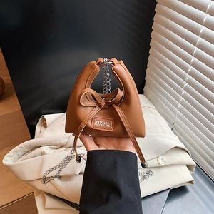 Close-up of caramel mini crossbody bag with leather bow and silver chain strap details
