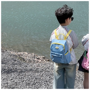 Rear view of a child wearing a blue and yellow backpack by the water during outdoors