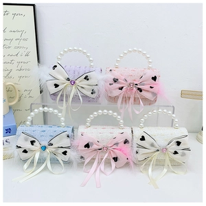 Five colors of tweed mini handbags with pearl handles and decorative bows displayed on a rack