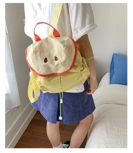 Detail of apple-shaped backpack with yellow body, beige flap, and red accents on model