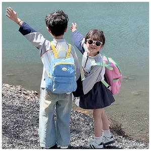 Outdoor shot of kids wearing pink and sky blue candy-colored backpacks by the lake
