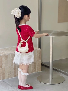 Detail showing a cream crescent handbag paired with a red polka dot dress on a child model