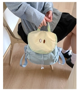 Close-up of light blue and beige nylon backpack with drawstring and flap closure