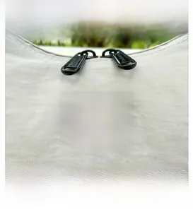 Detail view of the durable cream fabric bag featuring a black dual-zipper closure and logo
