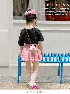 Toddler girl wearing pink bow handbag with plaid skirt and black t-shirt outdoors