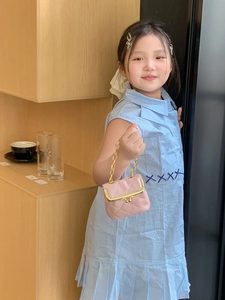 Detail showing pink quilted mini handbag with gold chain held by girl in blue dress