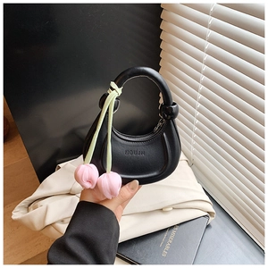 Close-up of black leather crescent bag with pink floral charm in a minimalist setting
