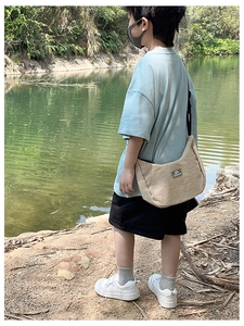 Outdoor view of child wearing a beige crescent crossbody bag with adjustable strap