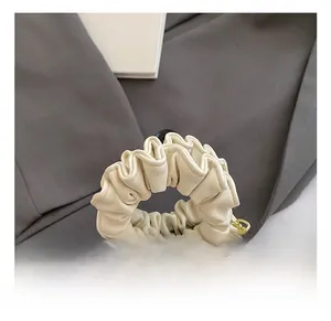 Detailed close-up of cream-white pleated handbag with golden chain and pink bow accents