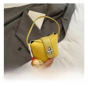 Detail einer gelben gewebten Beuteltasche mit Lederklappe und süßem Puppenanhänger