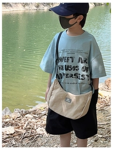 Outdoor view of child model wearing a beige canvas crossbody dumpling bag for kids