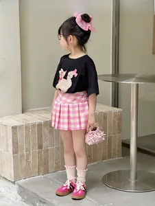 Detail view of girls' black T-shirt with cat print and pink bow paired with plaid skirt