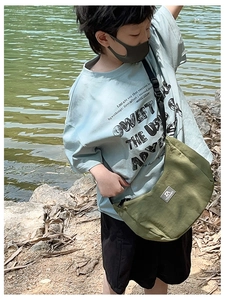 Detail of army green canvas crossbody bag with logo patch against outdoor lake background