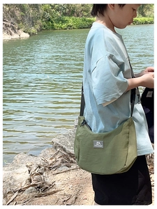 Olive green nylon crescent crossbody bag worn by a child on an outdoor riverbank