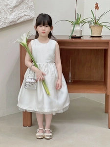 Close-up of white satin sleeveless dress with fluffy tulle hem and silver quilted bag