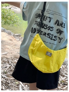 Outdoor side view of a yellow nylon half-moon crossbody bag with adjustable black strap