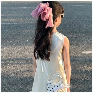 Vue de dos d'une fille portant un grand nœud de cheveux en mousseline rose au soleil