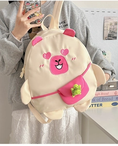 Detailed view of beige cartoon backpack with pink mini bag and turtle plush charm
