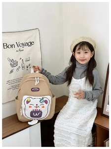 Detail view of beige kids backpack with cute cartoon cat pocket and side storage pouch