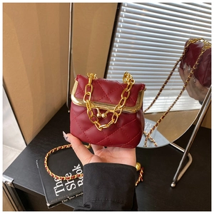 Close-up of wine red quilted girls handbag with gold chain strap on a black table