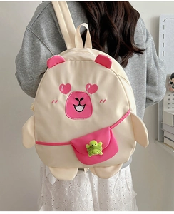 Detail of cream cartoon backpack featuring animal face design and green turtle pendant