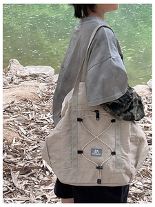 Close-up of beige nylon travel bag showing front zipper pocket and elastic drawstring details