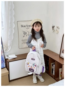 Detail showing white kids backpack with purple accents and cute bear pattern on front pocket