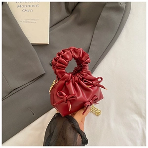 Detail of red cloud handbag with bow accents and pleated handle on a grey blazer