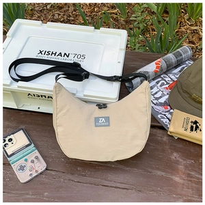 Lifestyle shot of beige nylon half-moon crossbody bag with adjustable strap and brand label