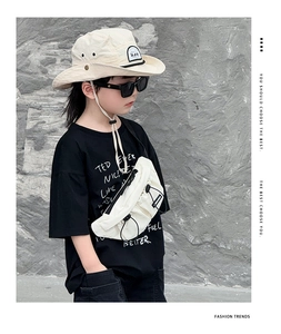 Detail of a white crossbody chest bag on a black t-shirt and beige bucket hat for kids
