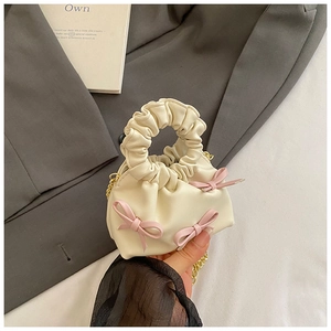 Detail of a creamy white cloud mini bag with pink bows and golden chain strap
