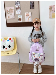 Girl wearing light purple school backpack with cartoon bear pocket in a cozy setting